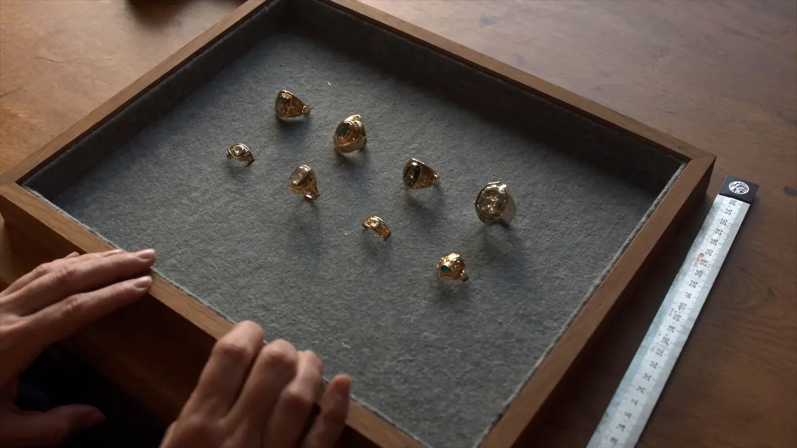 A grey felt jeweller's tray on a wooden counter holding eight gold rings, with a folding steel rule laid alongside them.